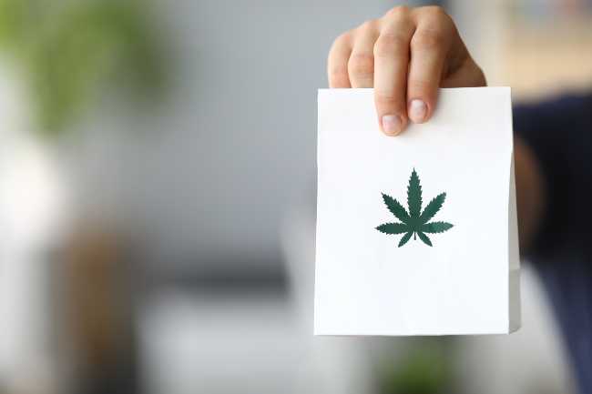 Image of a hand holding a white paper bag cannabis delivery with a marijuana leaf on it