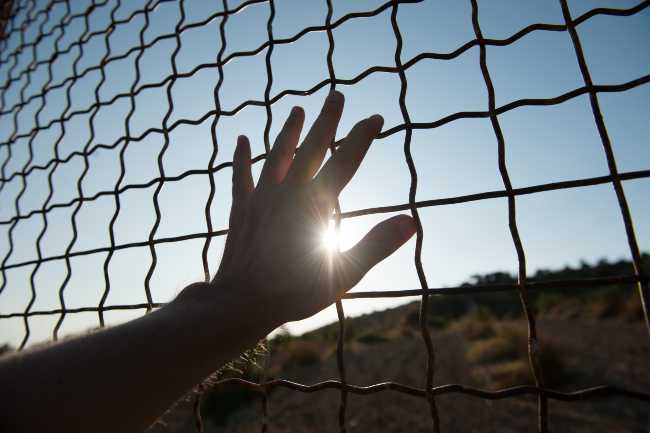 Image of a hand on a chain fence inside of a prison.