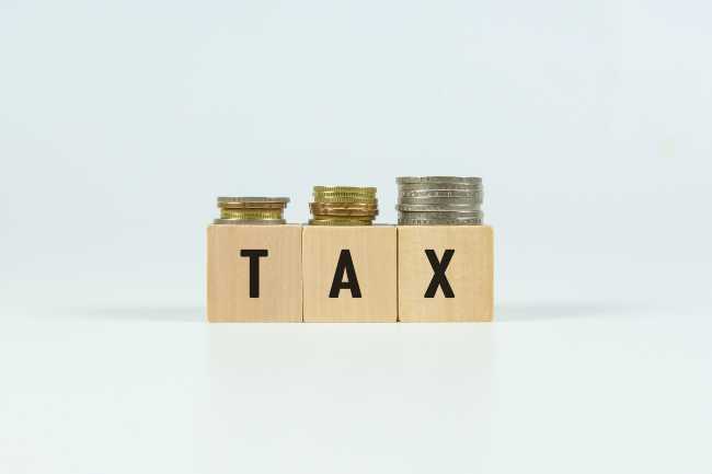Three block letters spelling out Tax with coins stacked on top of them.