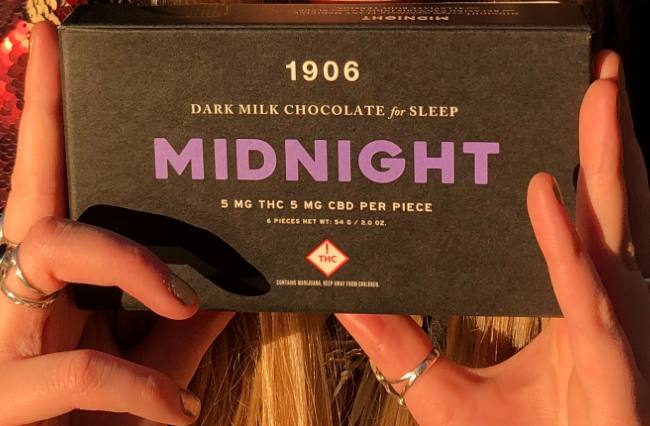 Hands holding a box of 1906 Midnight Gems which is black with purple font