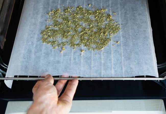 Image of someone putting a tray with white parchment paper and weed on top, into the oven