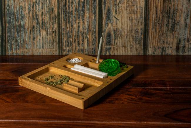 Image of an oak colored rolling tray with grooves for white papers, green grinders, and pre-rolled joints.