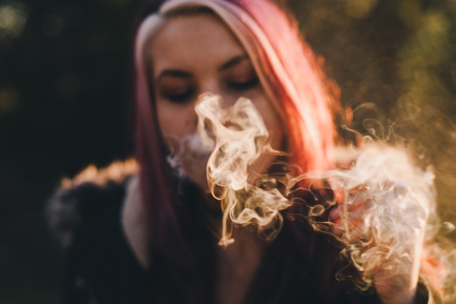 a woman with pink hair blows out a cloud of smoke