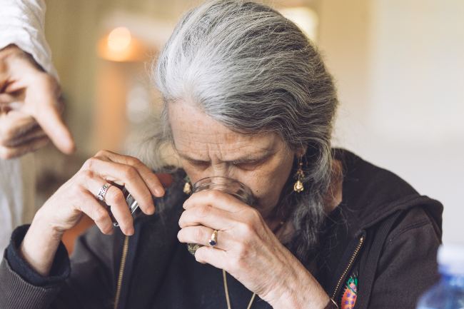 An women with light and dark grey hair smelling a cannabis jar