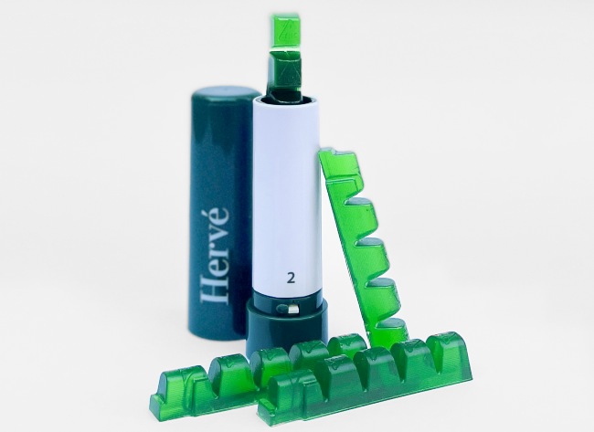 An image of Herve hard candy edibles which are a bright green bricks connected at the bottom and stored in a lip stick-like container that has a white inside and a dark green cap