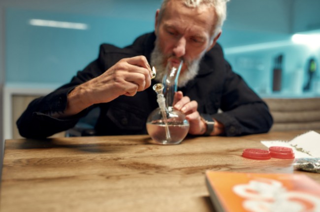 An older man smoking a bowl out of a bong