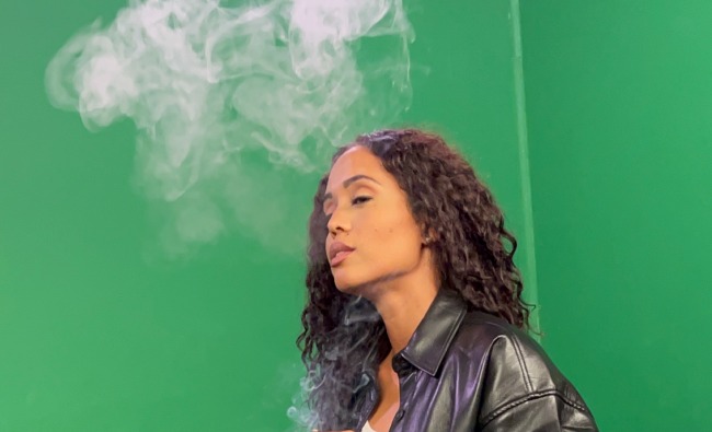 Tammy Pettigrew is standing with her eyes closed with a smoke cloud rising above her wavy black hair