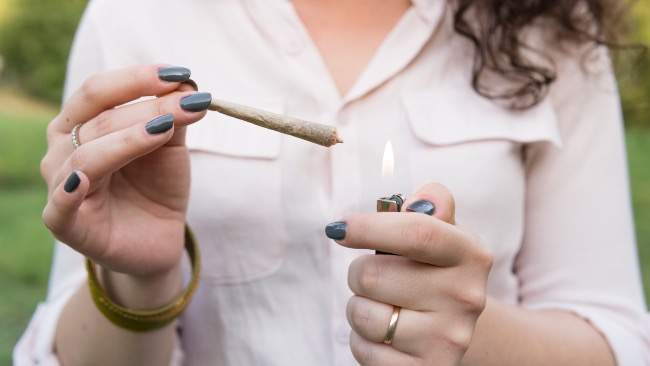 a woman in an off-white blouse lights a joint