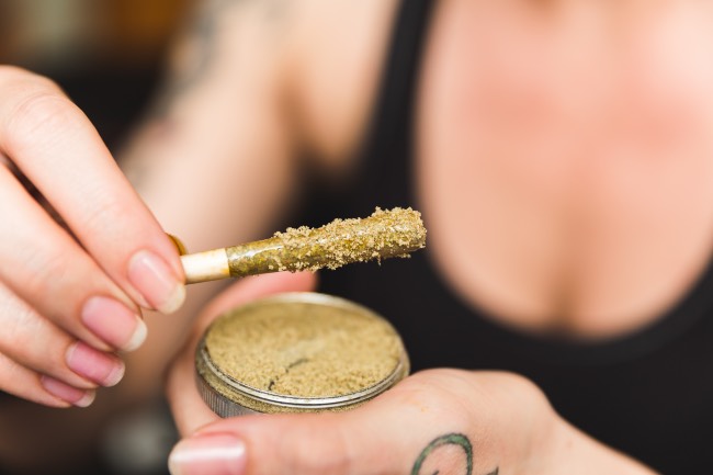 a woman in a black tank top holds a joint that has been dipped in kief