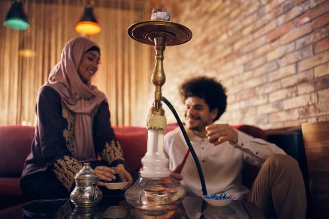 a muslim couple, sitting on a couch, shares a hookah