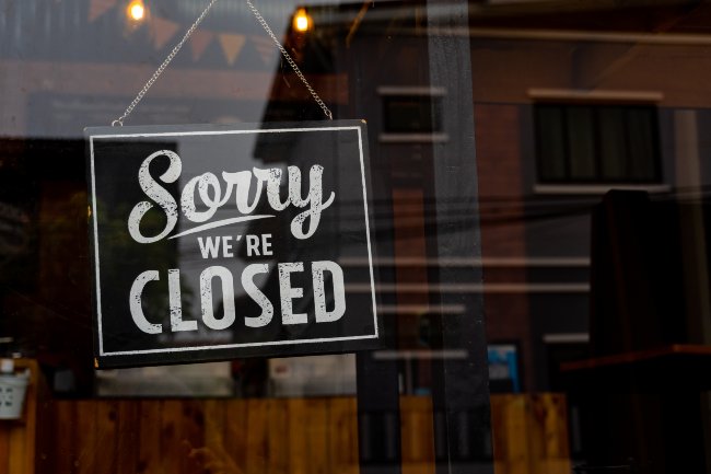 Une fenêtre avec un panneau noir suspendu par une ficelle indiquant « Désolé, nous sommes fermés ».