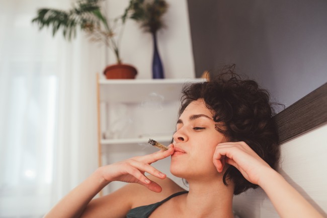 a woman with short dark hair smokes a joint while laying in bed