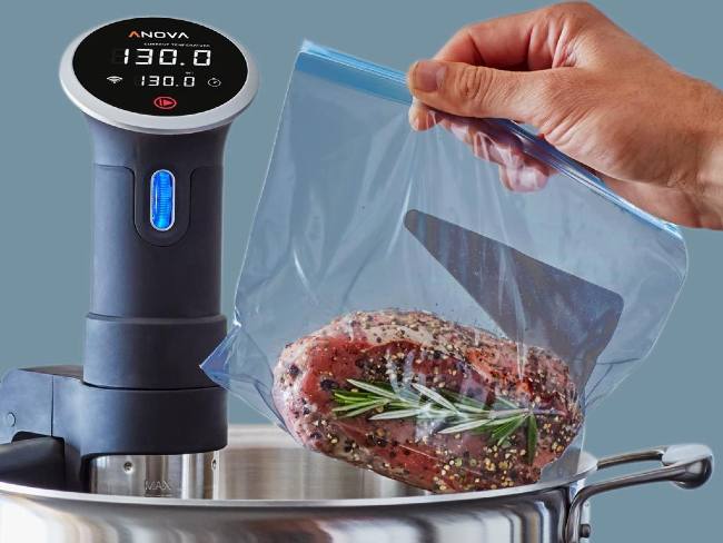 A plastic bag with red meat inside going into a metal pot that has a Sous Vide tower sticking out reading 130 as the temperature.