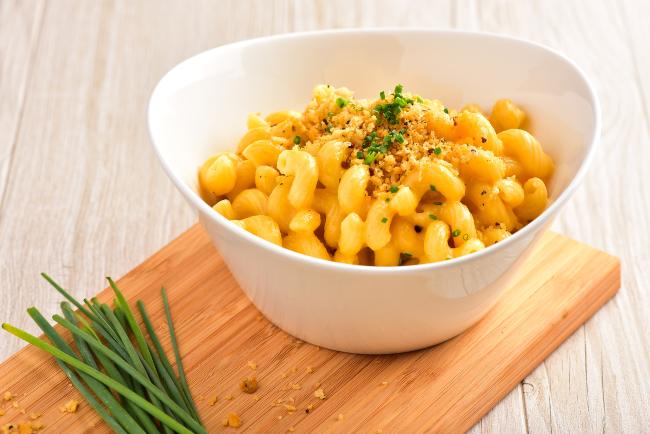 a white bowl filled with cavatappi mac and cheese topped with breadcrumbs, a bundle of chives laying next to it