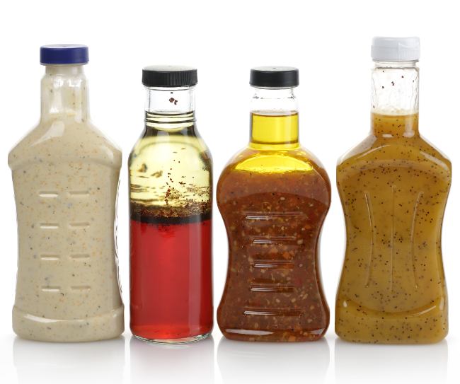 Four salad dressings are in a line in clear containers, including caesar and red wine vinaigrette.