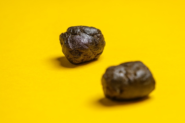 Two balls of brownish, black hash that is in front of a yellow background.