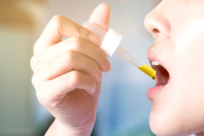 a woman drops a drop of CBD tincture under her tongue