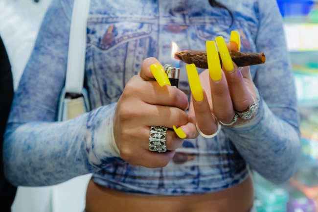 Hands rolling blunt with long, yellow nails and denim clothes on