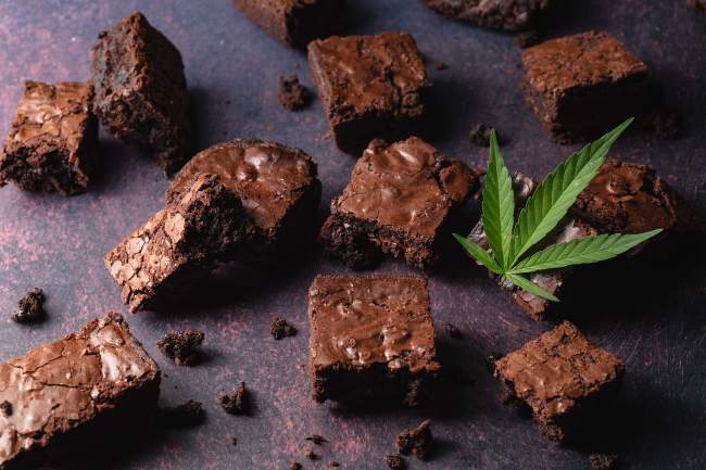 Brownies dispersed on a gray slat with pot leaves surrounding them