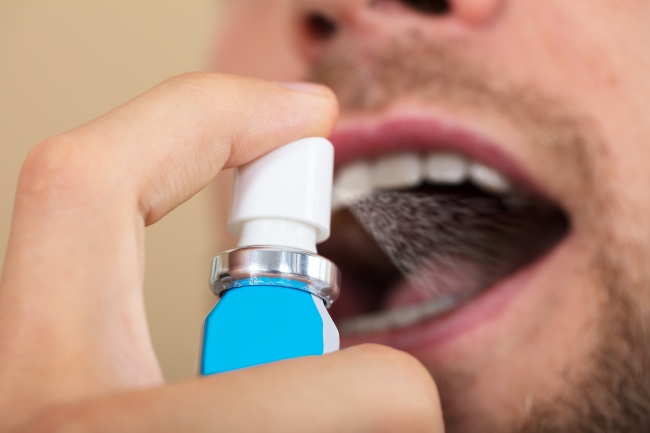 Man using a mouth spray with his mouth open.