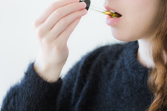 Woman raising a cannabis tincture to her mouth with yellow liquid inside of the dropper