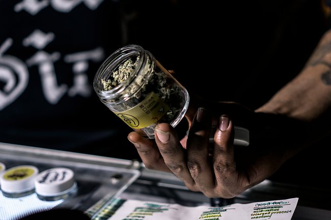 Hand holding a clear cannabis jar and slighting tipping it forward to show of the green buds inside
