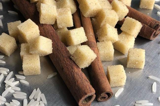 Small, tan cubes that are lying on top of brown cinnamon sticks and white rice.