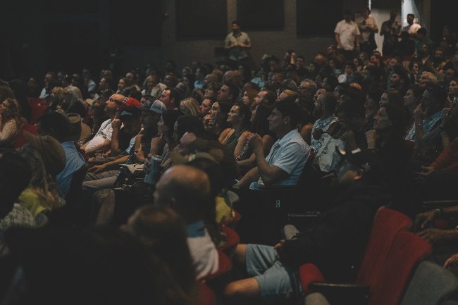 People sitting in an audience in a theatre listening to a speaker